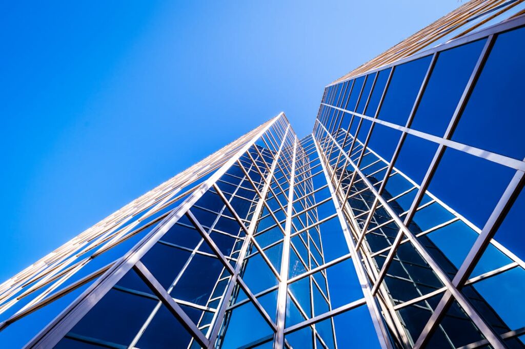 Low-angle view of a modern glass skyscraper with geometric blue panels and white framework against a clear blue sky.
